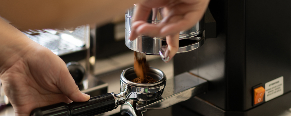 Barista grinding fresh coffee bean into portafilter for espresso.