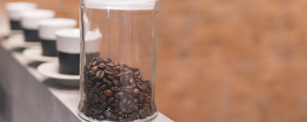 close up roasted coffee bean in clear container with ceramic cup