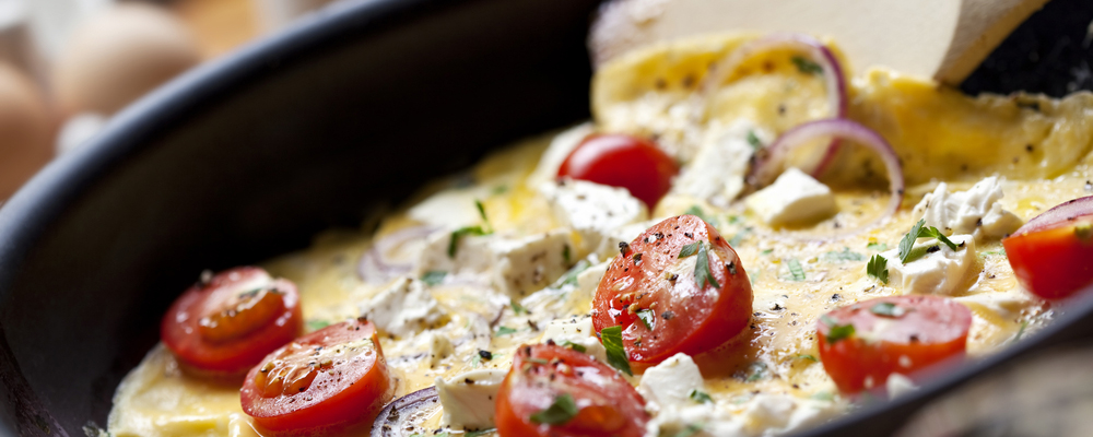 Cooking omelet in a pan, ready to serve.  With Cherry tomatoes, red onion, goat's cheese and parsley.  Shallow DOF.