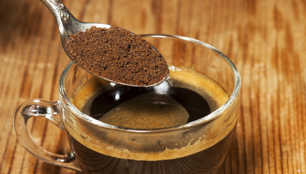 Glass coffee cup and spoon with instant granulated coffee on old wooden background.