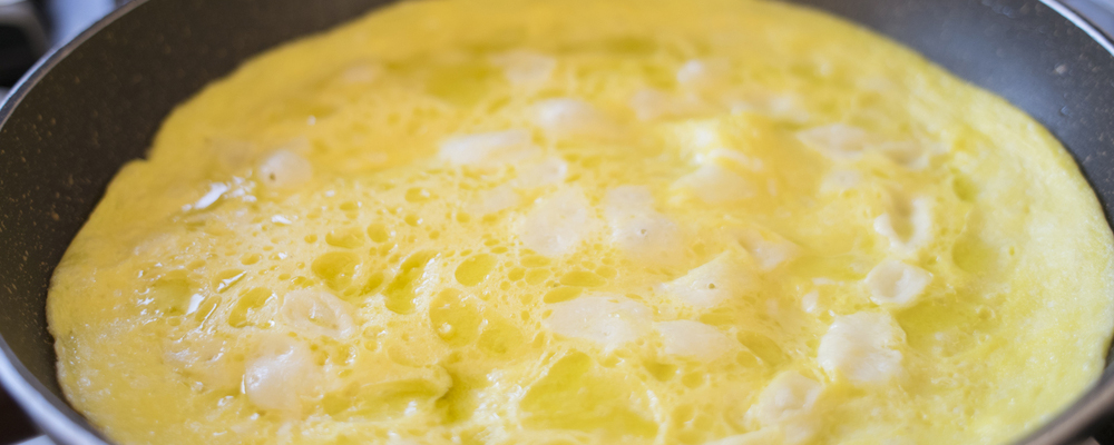 beaten eggs in pan with parmesan pieces to make an omelette