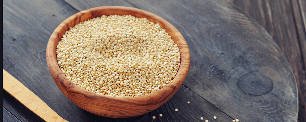 Raw quinoa seeds in the wooden bowl on wooden background closeup