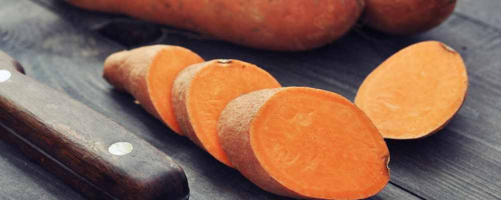 Raw sweet potatoes on wooden background closeup