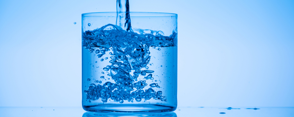 Toned image of water pouring in glass on blue background
