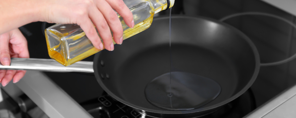 Closeup of woman pouring oil on frying pan
