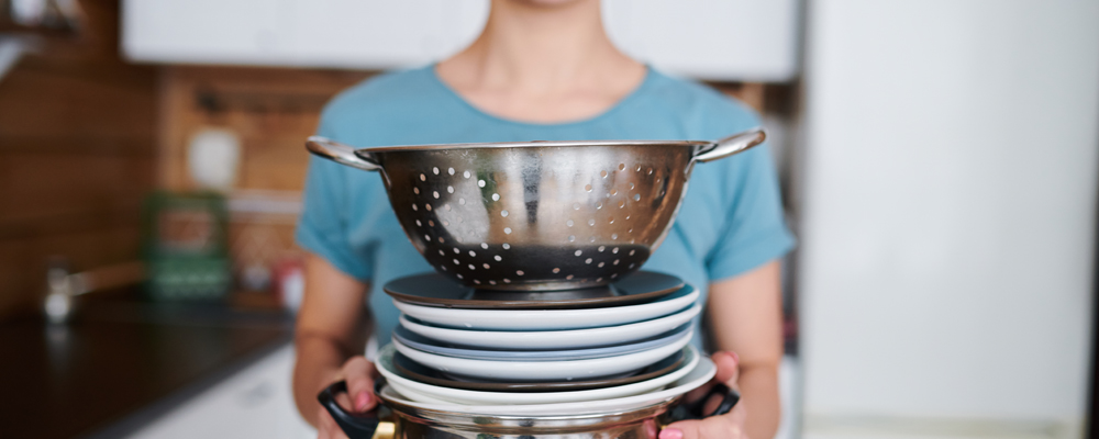 Young housewife holding stack of clean dishes and kitchenware in front of camera