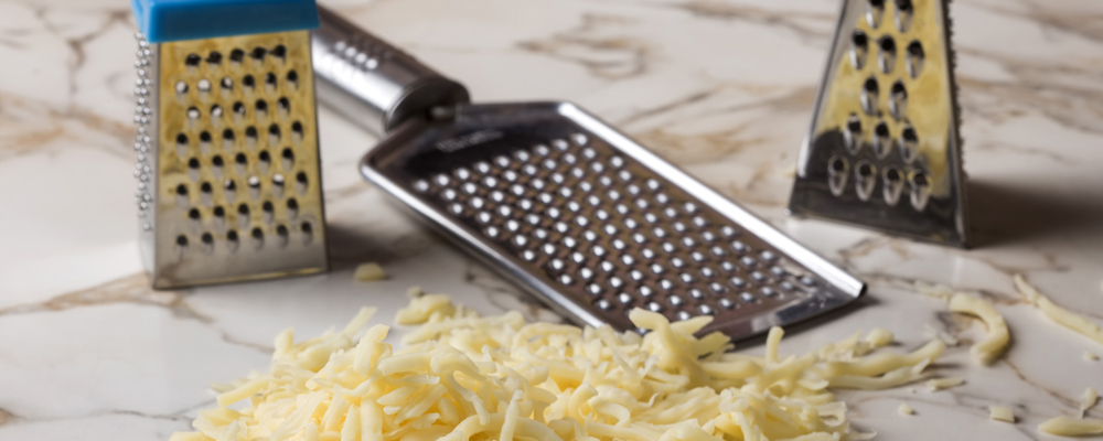 Grated mix cheese on table and three stainless steal graters in background