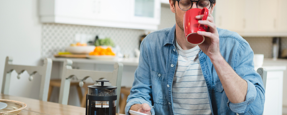 Man using mobile phone while having coffee in kitchen at home