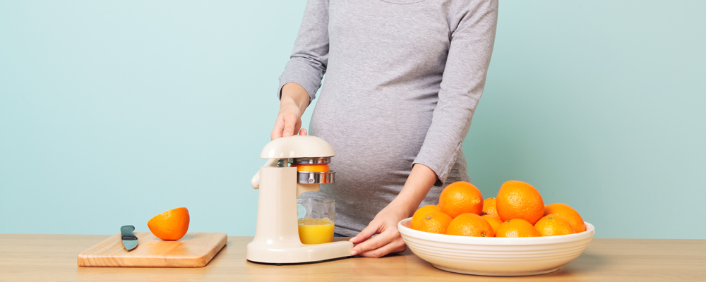 Pregnant woman making fresh orange juice.