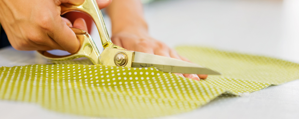 Close up of hands of unrecognizable tailor woman cutting green dotted fabric with scissors