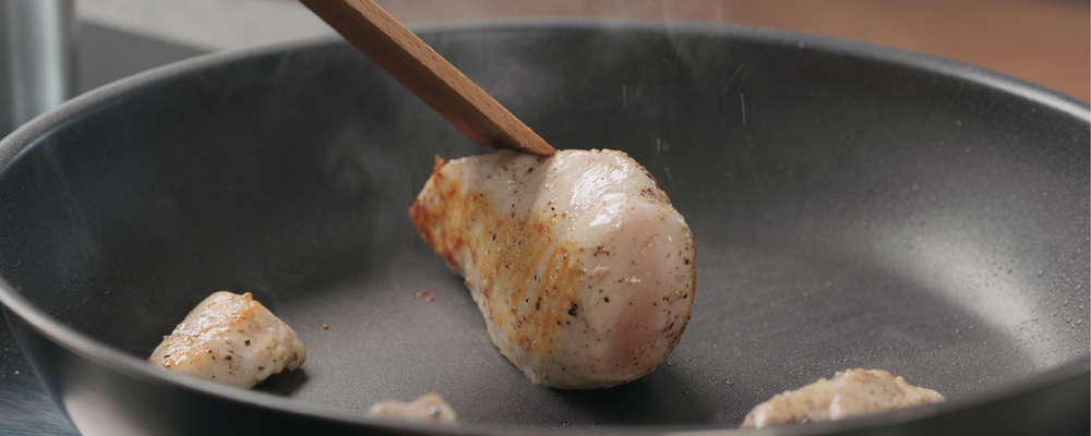 man hand turn over chicken fillet on non stick pan with wood spatula acloseup, wide photo
